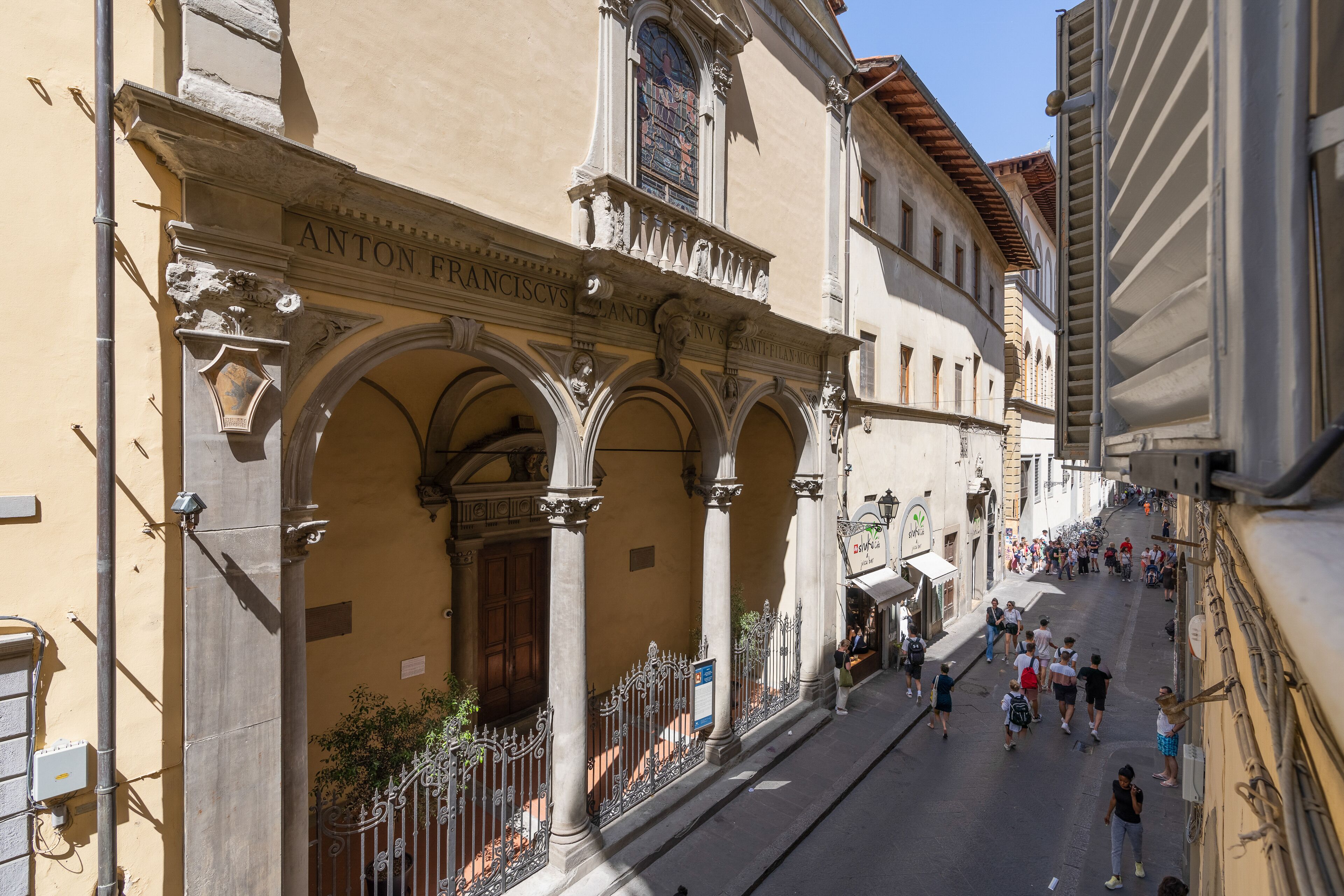 Una calle con un edificio identificado como "ANTON FRANCSIS" y una verja de hierro forjado.