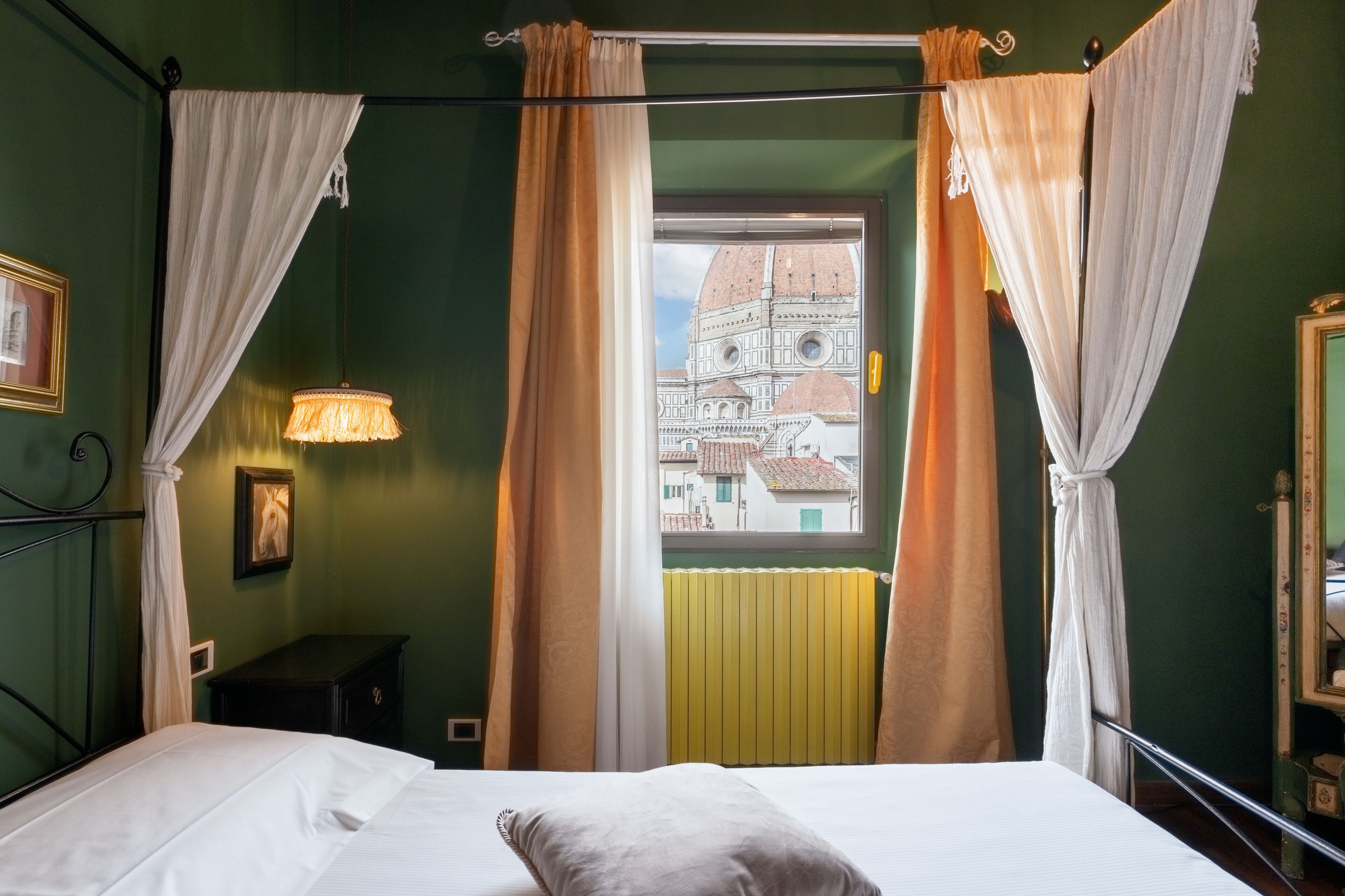 Um quarto com uma cama, janela com cortinas, luminária e radiador.