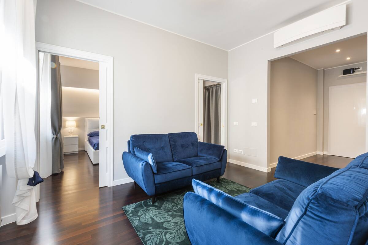 A modern living room with a blue sofa, a green patterned rug, and hardwood flooring.