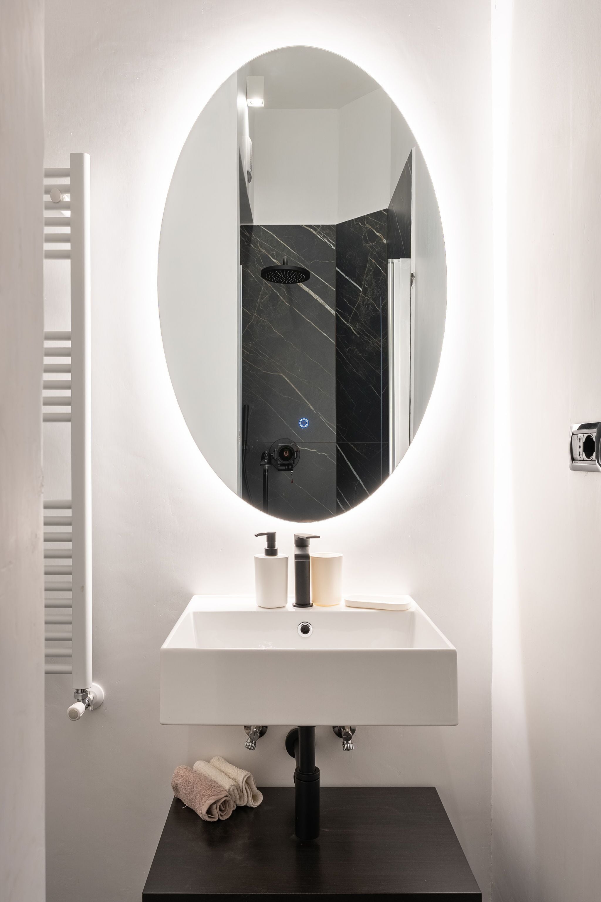 A bathroom with a white sink, a round mirror, and a black marble backsplash.