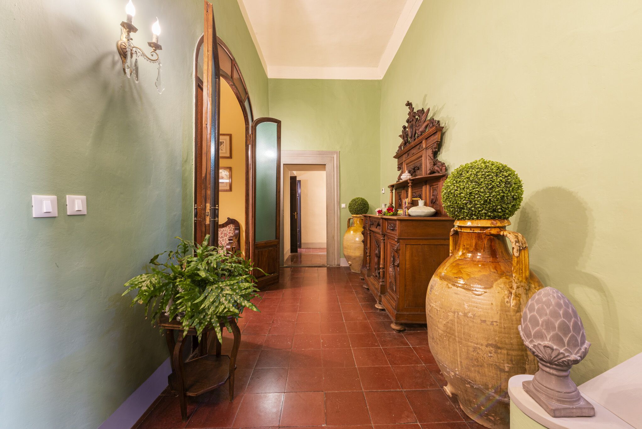 A hallway with a green wall, a wooden cabinet, a large vase, and a potted plant.