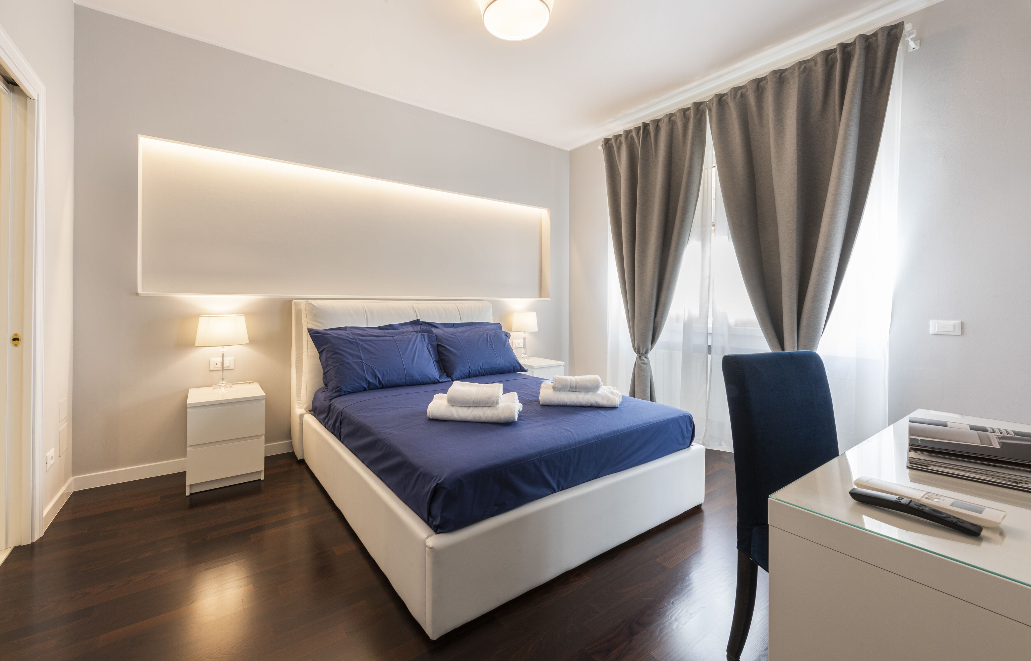 A modern bedroom with a large bed, bedside lamps, a desk, and a chair.
