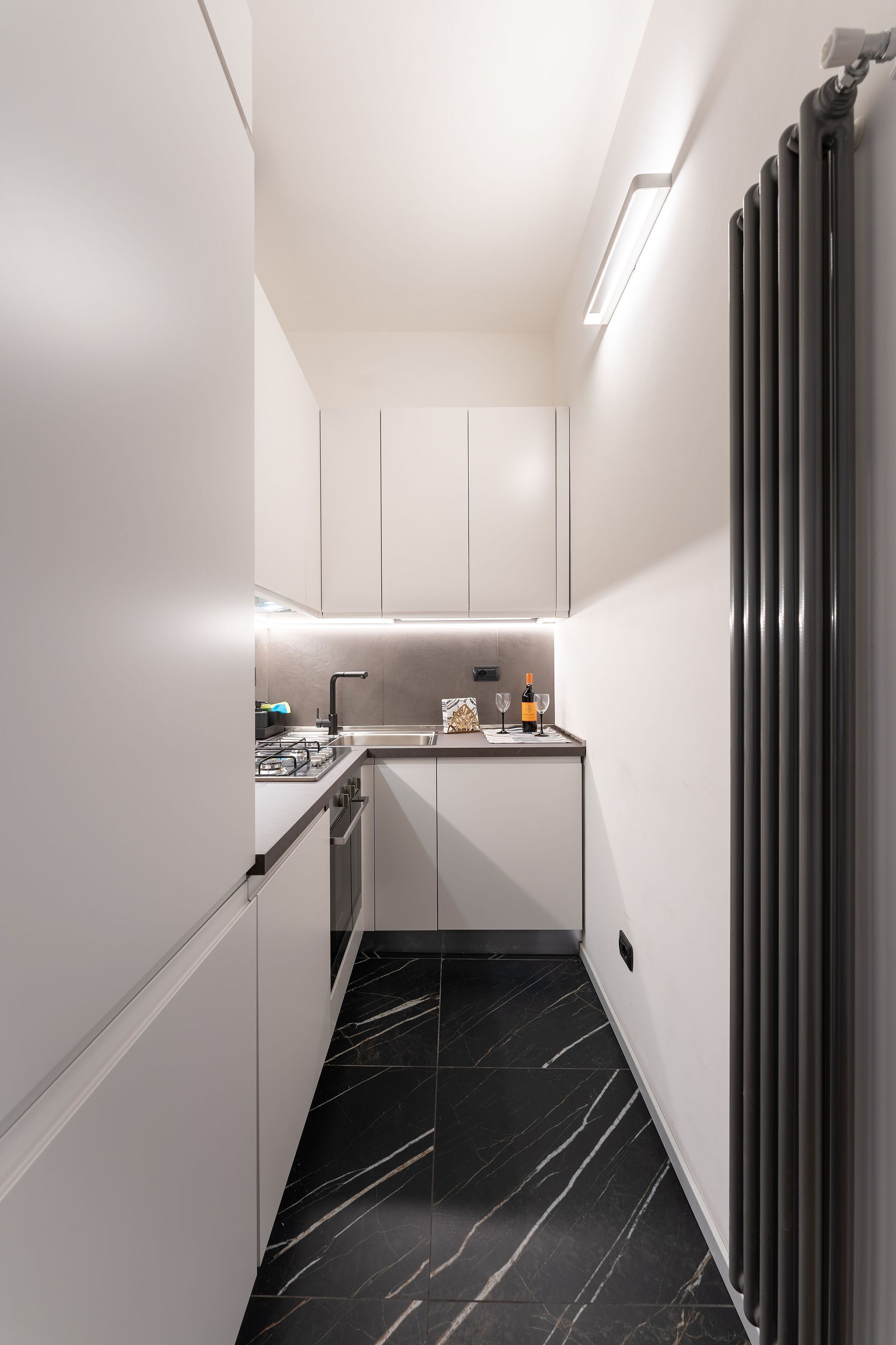 A narrow kitchen with white cabinets, a black marble floor, and a modern design.