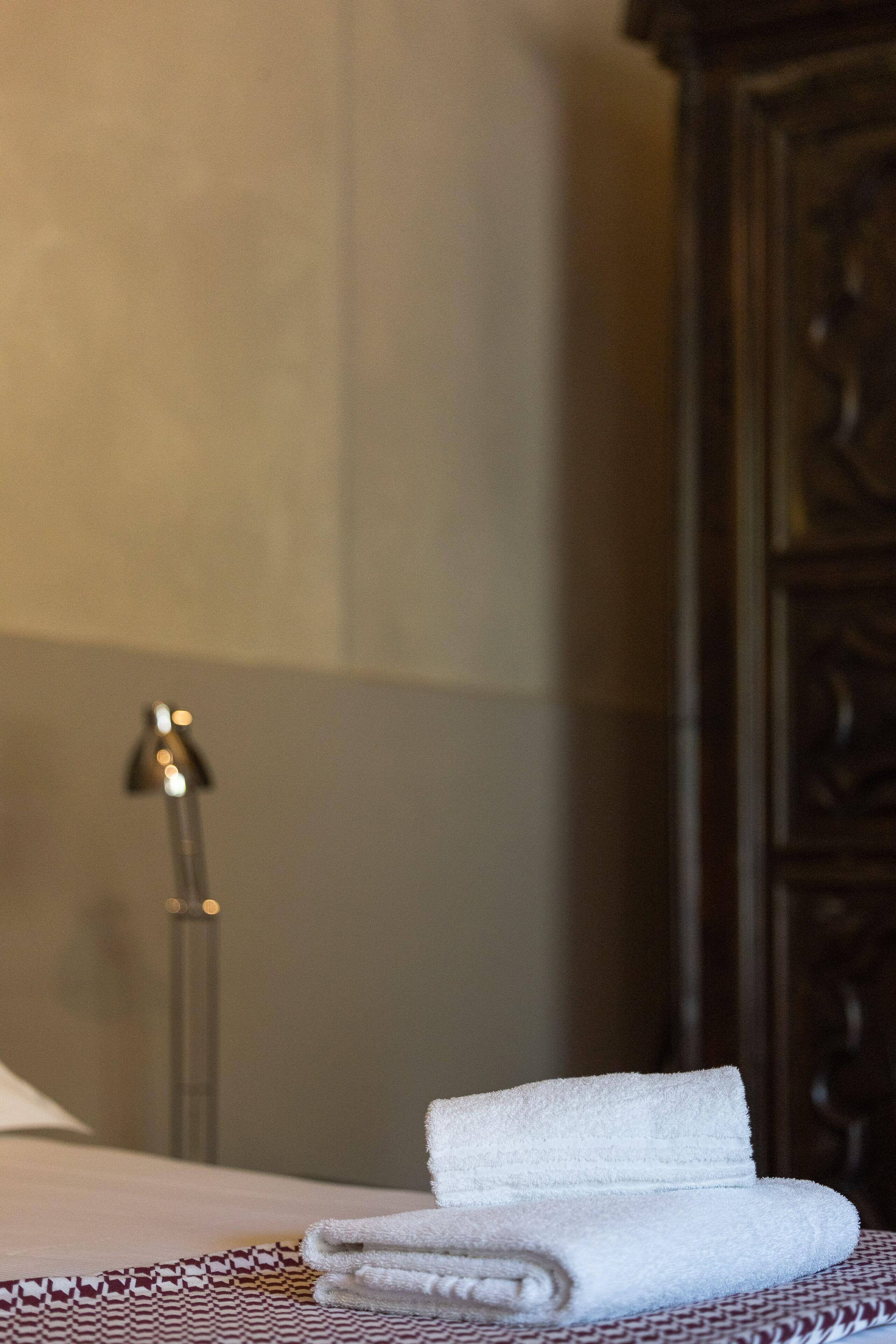 A neatly made bed with a folded white towel and a patterned bedspread.