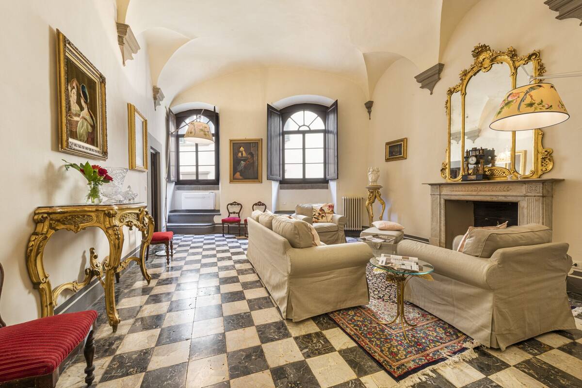 A checkered floor, a fireplace, and a sofa in a room with a high ceiling and arched windows.
