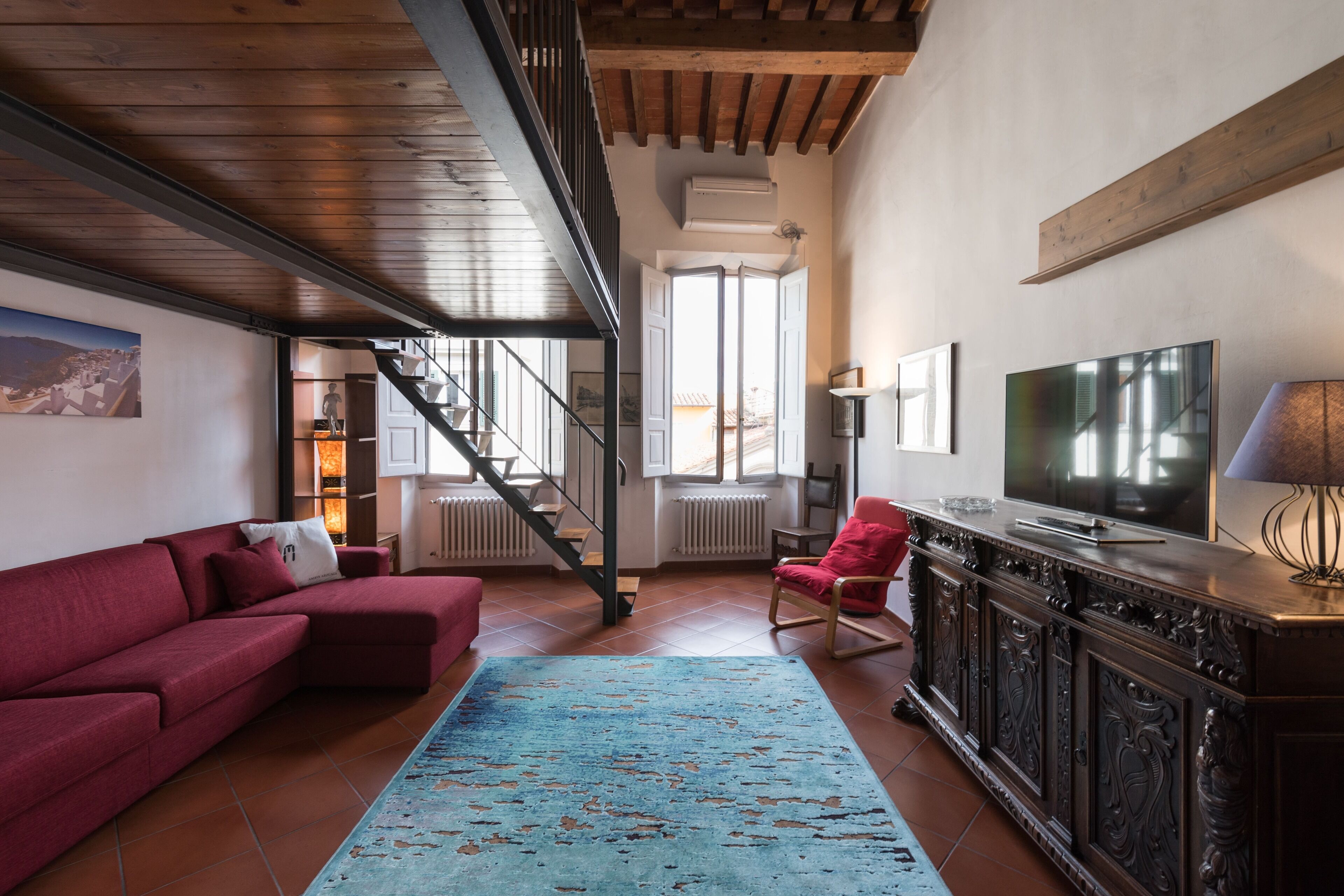 Ein Wohnzimmer mit einem roten Sofa, einem blauen Teppich, einem Fernseher und einer Treppe, die eine weitere Ebene hinaufführt.