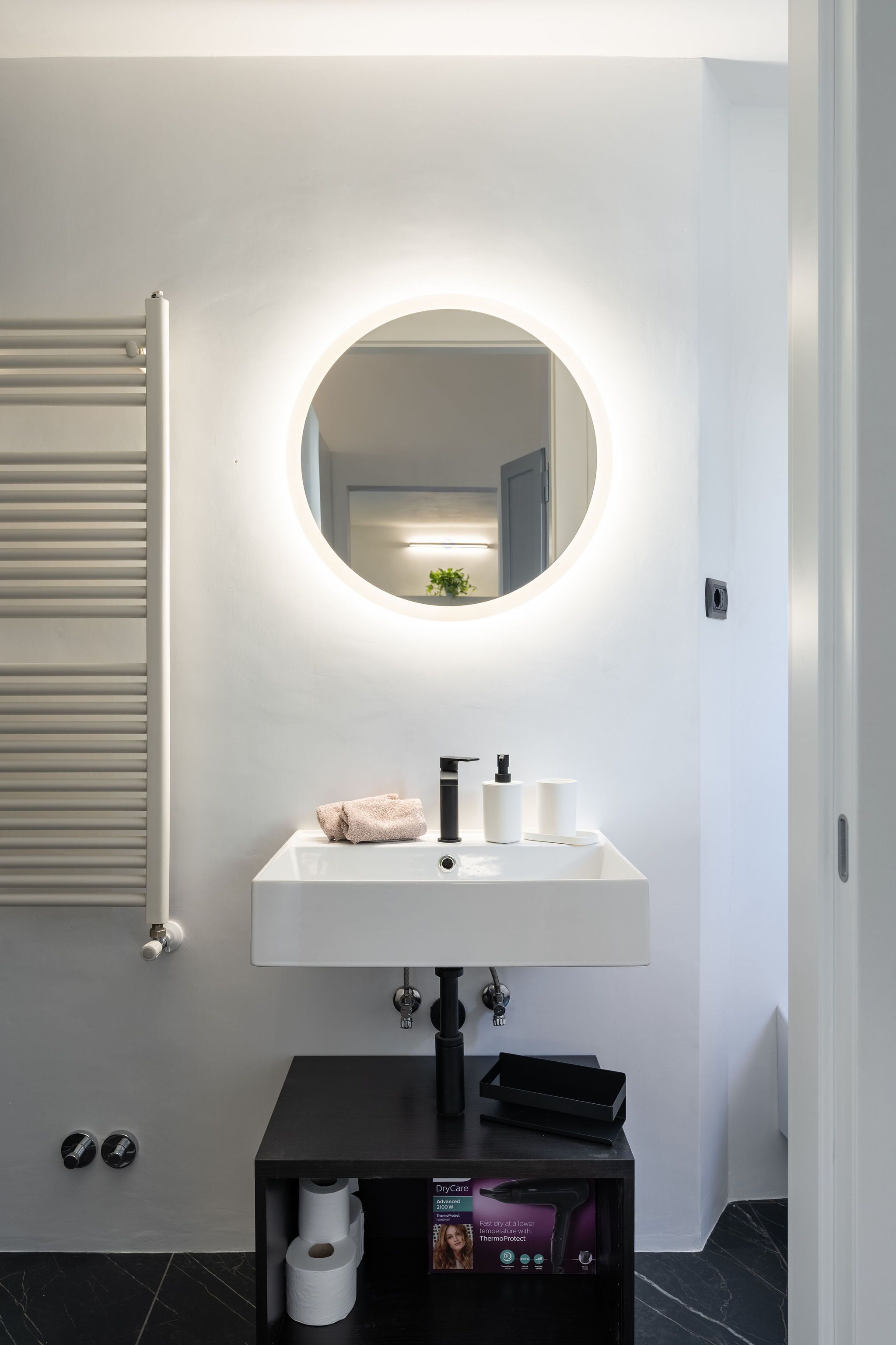 A modern bathroom with a white sink, a round mirror, and a towel rack.