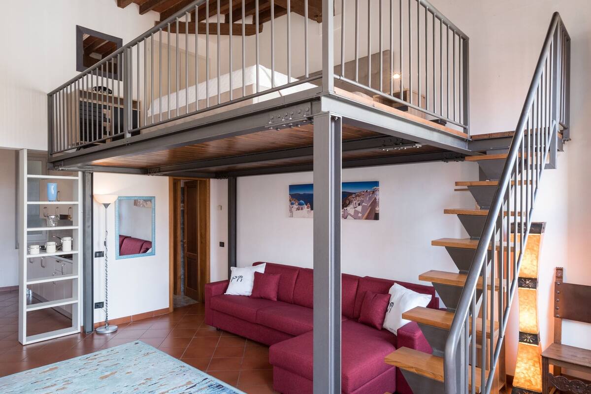 A spacious living area with a red sofa, wooden staircase, and a mezzanine level.