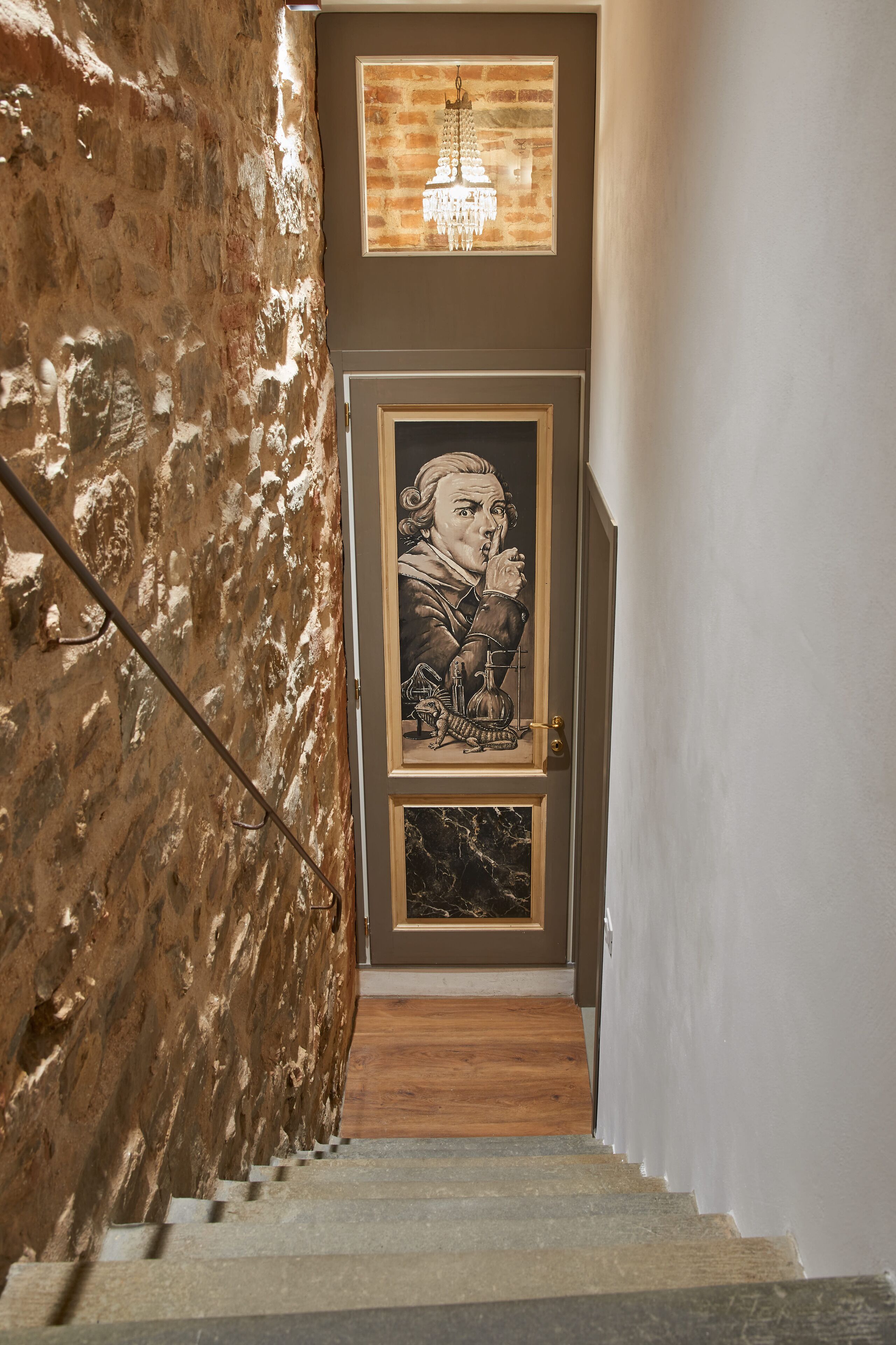 Un escalier avec un mur de marbre d’un côté et une porte ornée d’un portrait encadré.