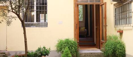 A courtyard with a wooden door, potted plants, and a small staircase leading to a room.