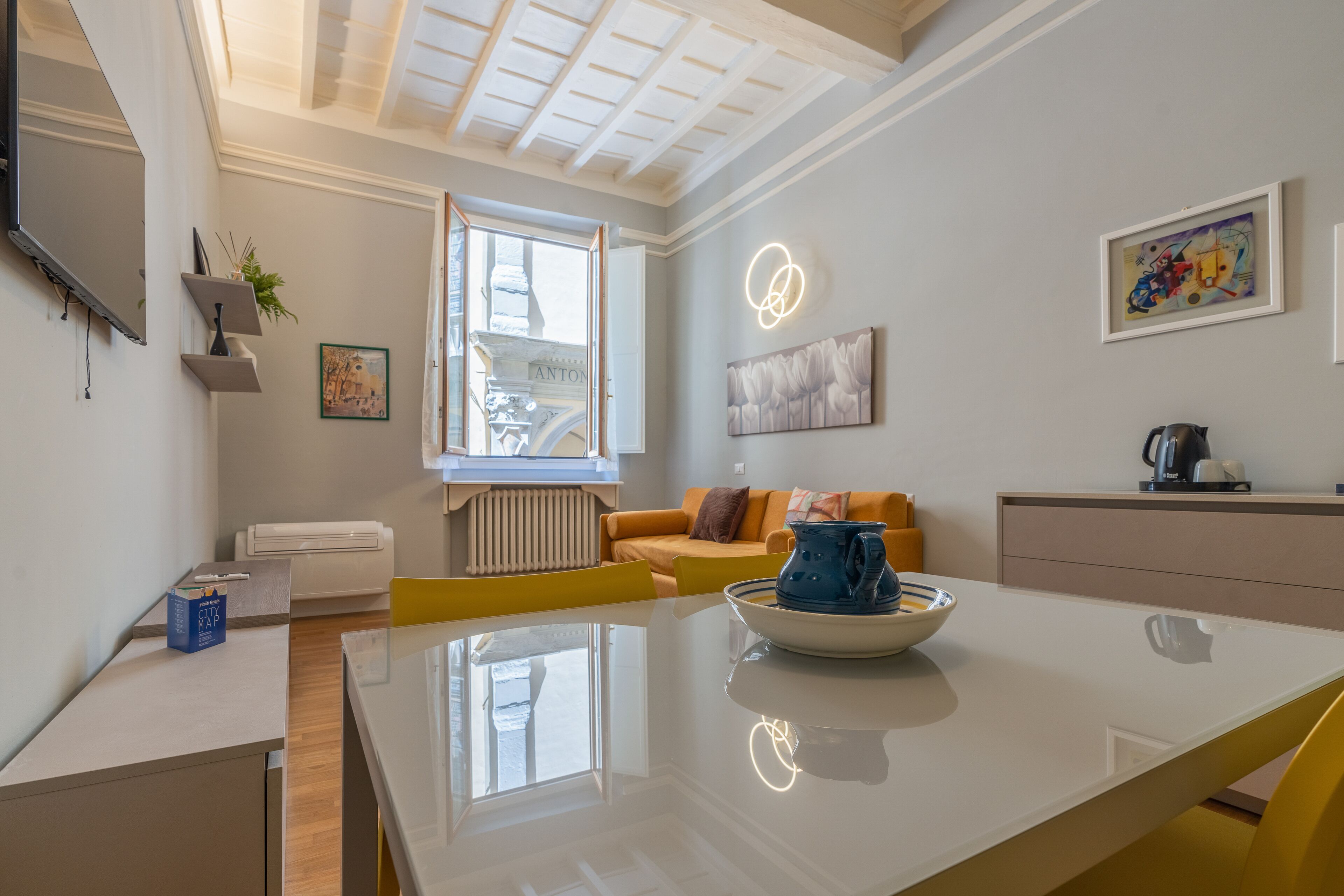 A modern kitchen with a dining table, a coffee machine, and a window with a view of the street.
