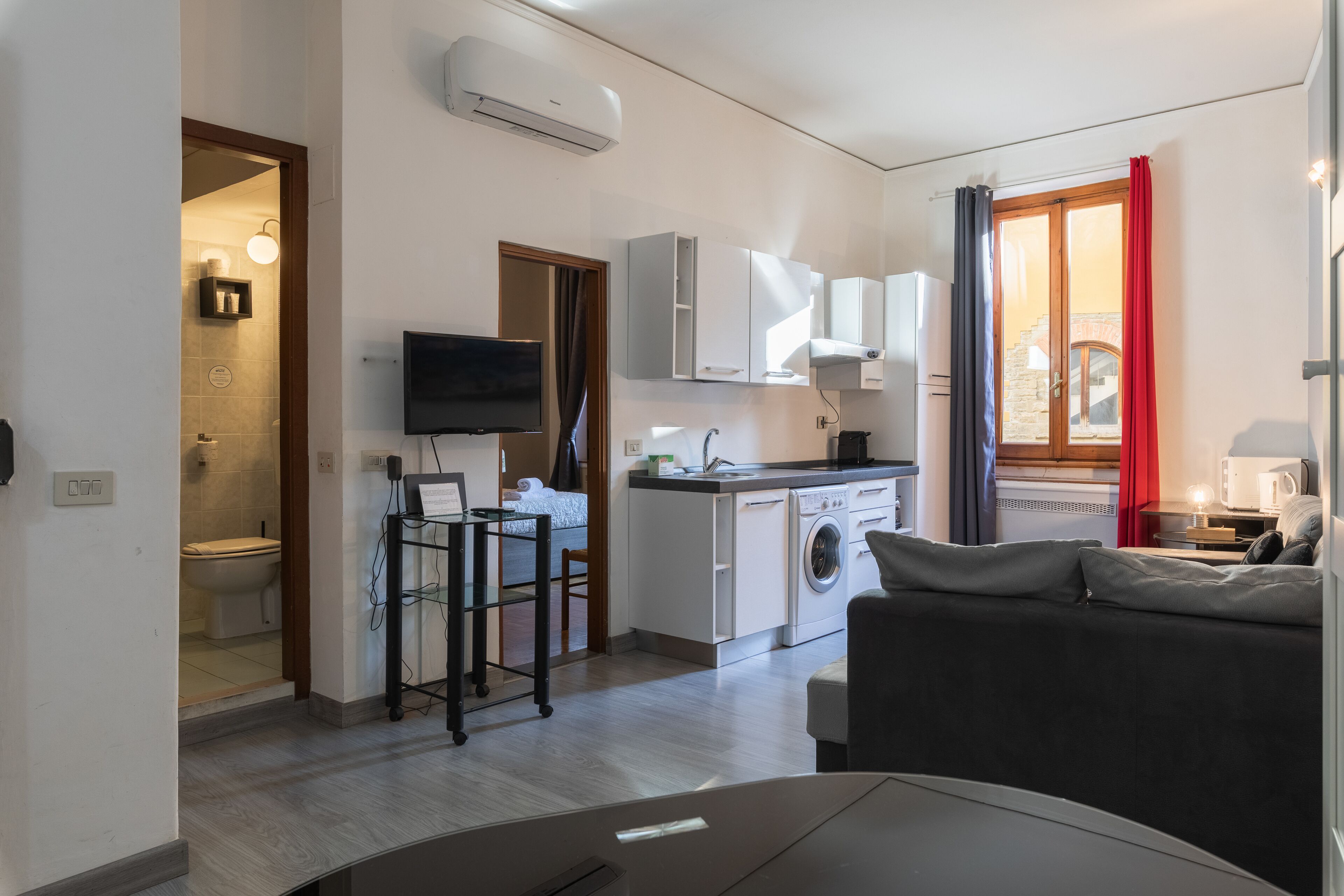 Un espace de vie compact comprenant un coin cuisine, un lave-linge, un téléviseur à écran plat et un canapé.
