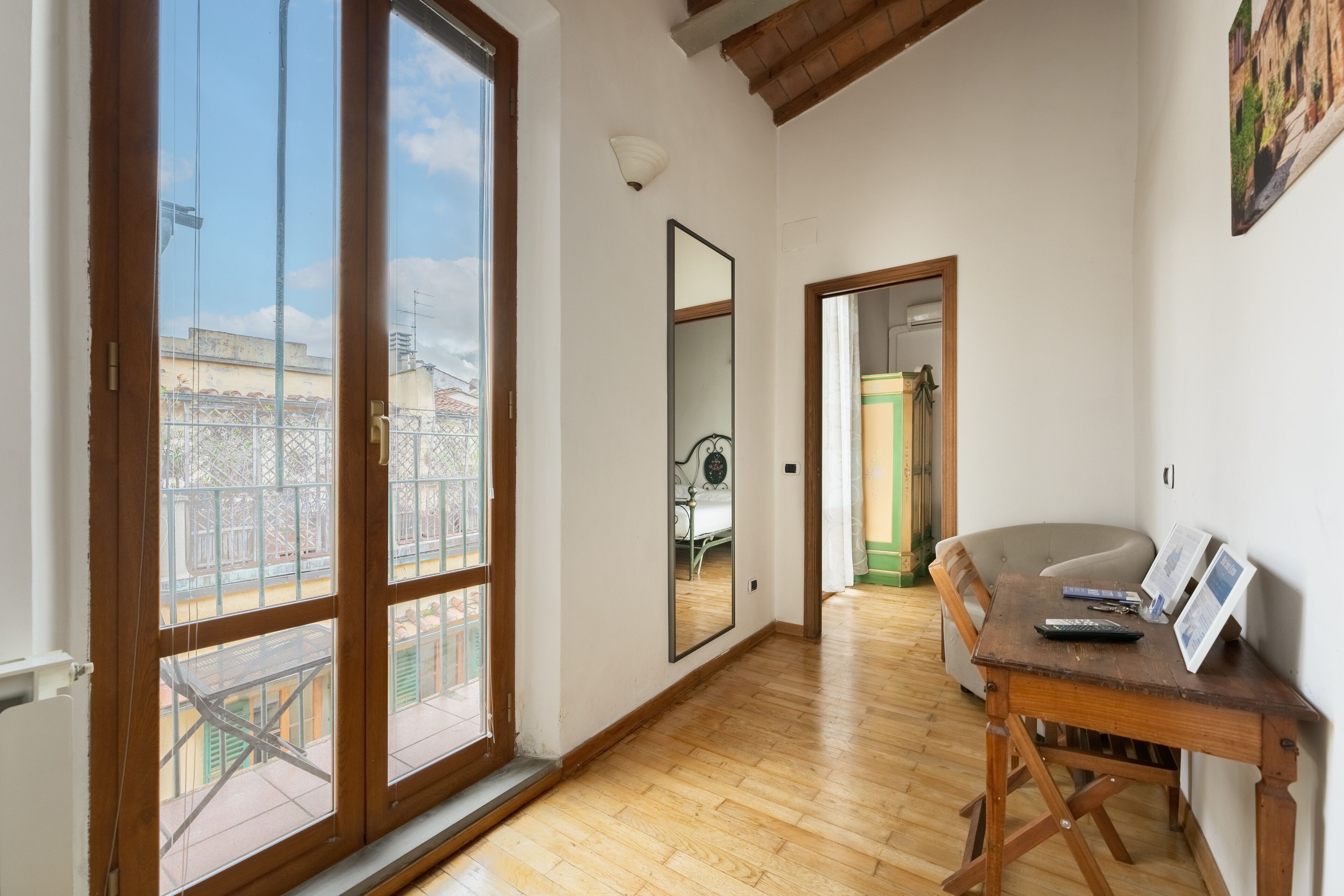 A room with large sliding glass doors, a wooden floor, a wooden desk with a chair, and a mirror on the wall.