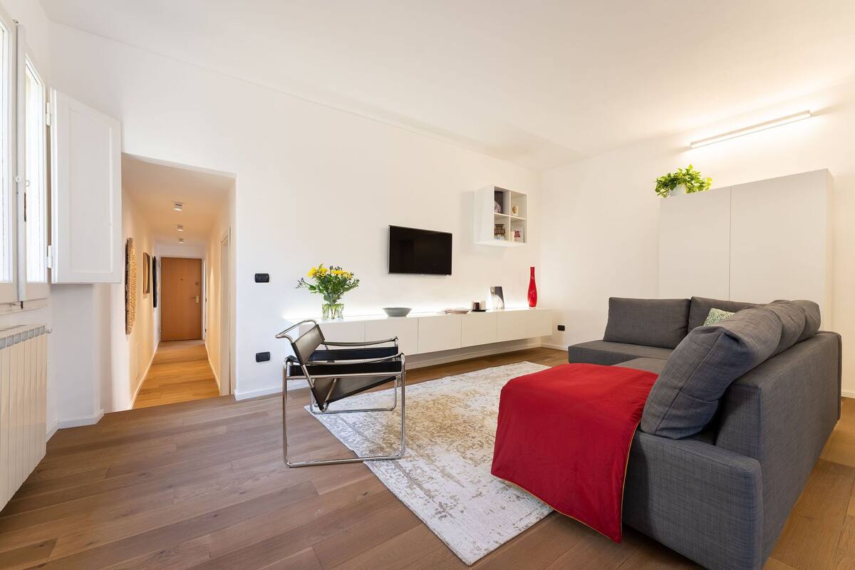A modern living room with a grey sofa, a red throw blanket, and a black chair.