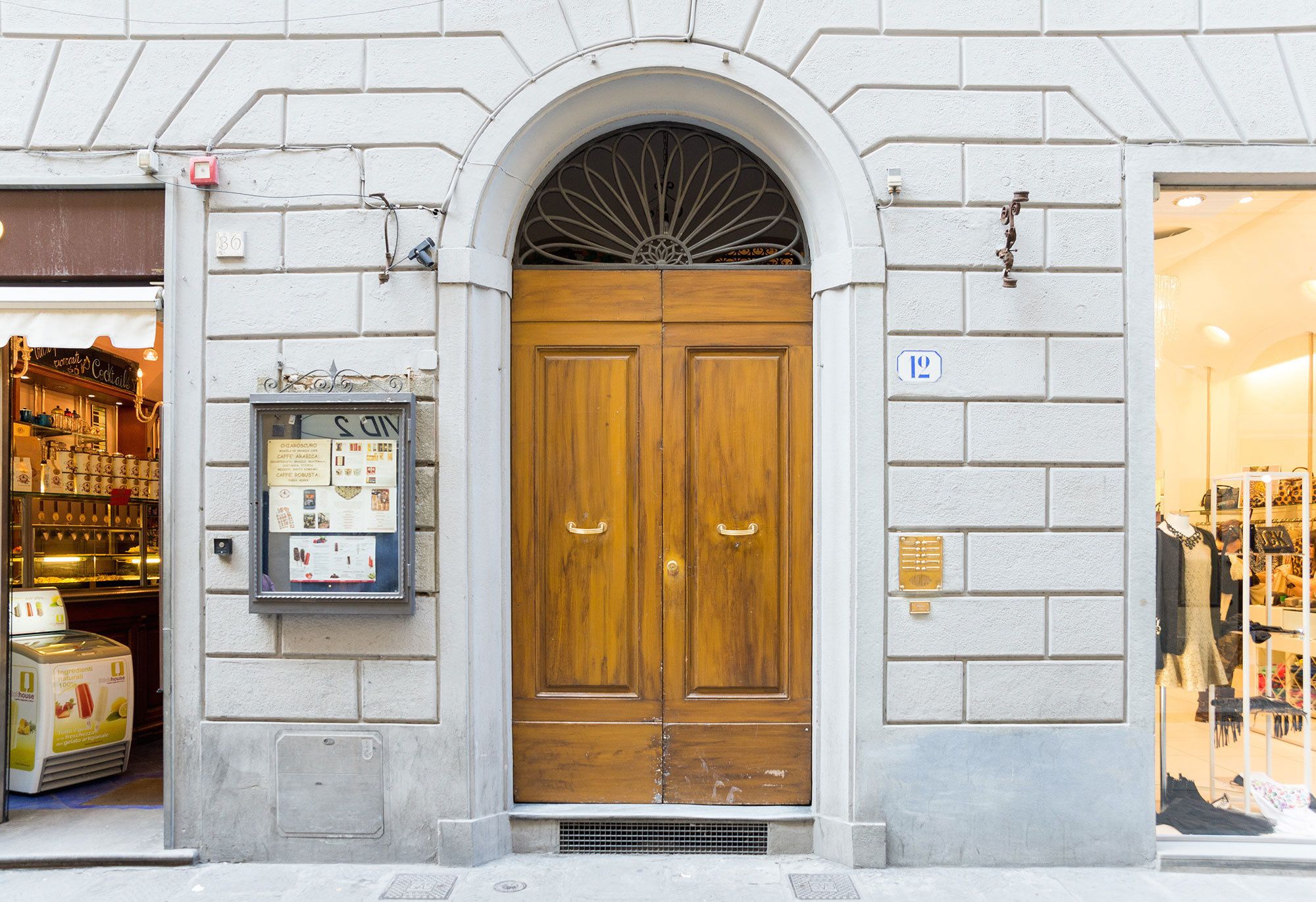 A building with a large wooden double door, a small window with a decorative metal grill, and a mailbox on the left side.