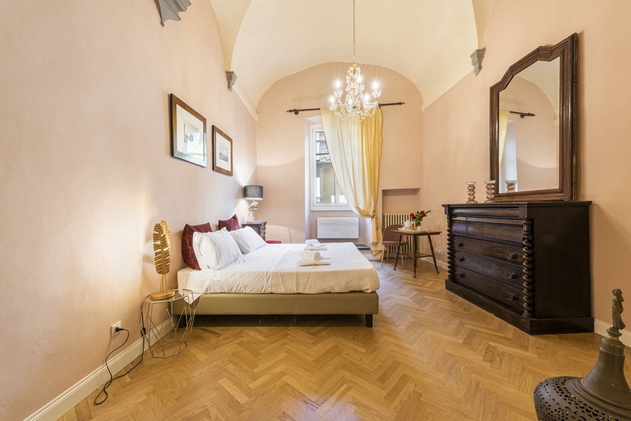 Une chambre à coucher avec un grand lit, une commode, un miroir et un lustre.