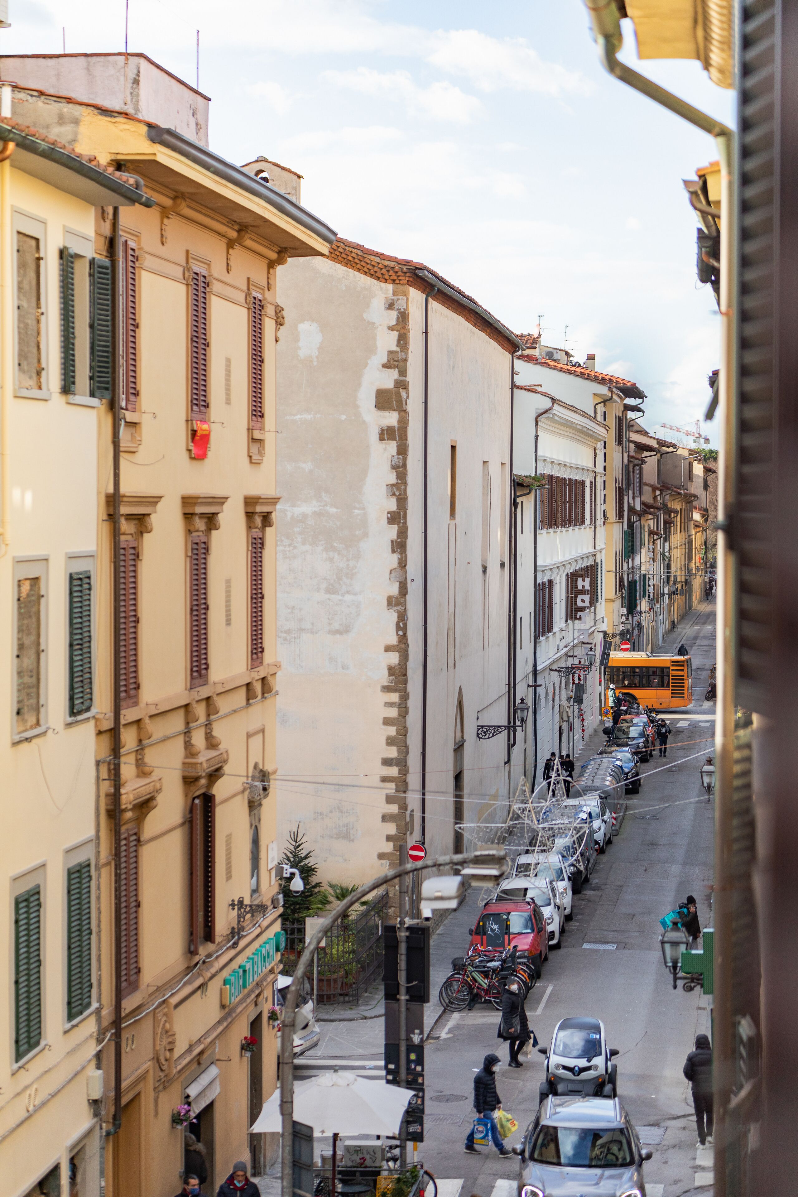 A narrow street lined with buildings, a yellow bus, parked cars, and bicycles.