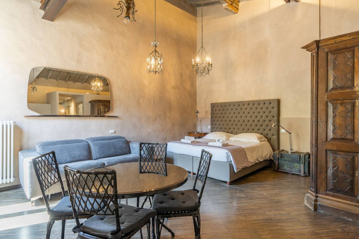 A modern living room with a round dining table, a sofa, and a bed with a tufted headboard.