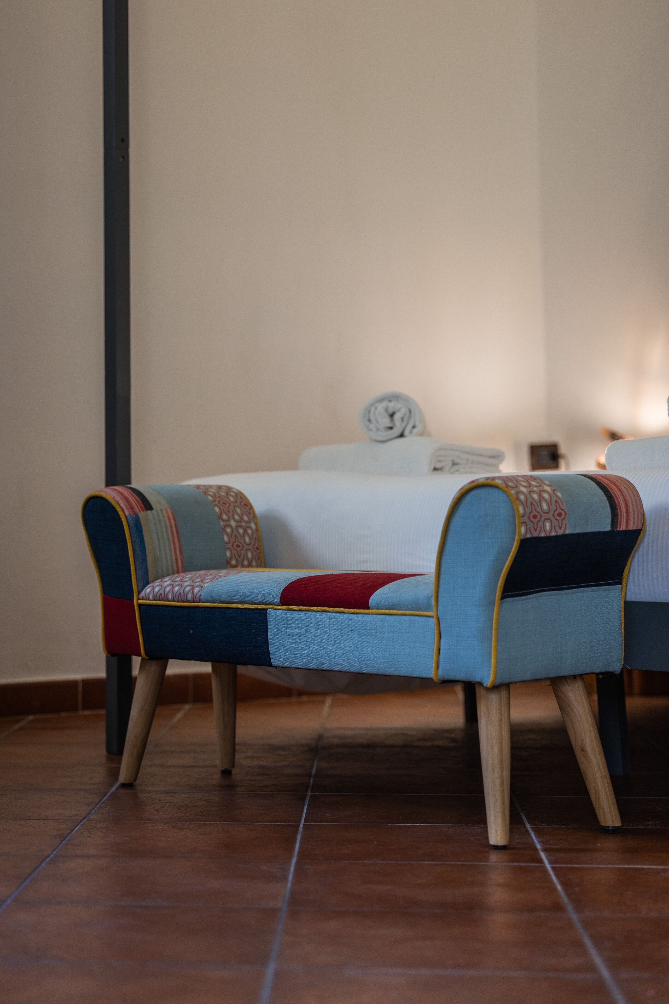 A room with a bed, two upholstered chairs with patterned cushions, and a tiled floor.