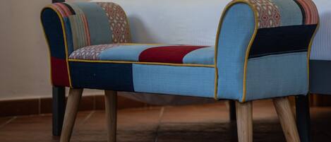 A room with a bed, two upholstered chairs with patterned cushions, and a tiled floor.