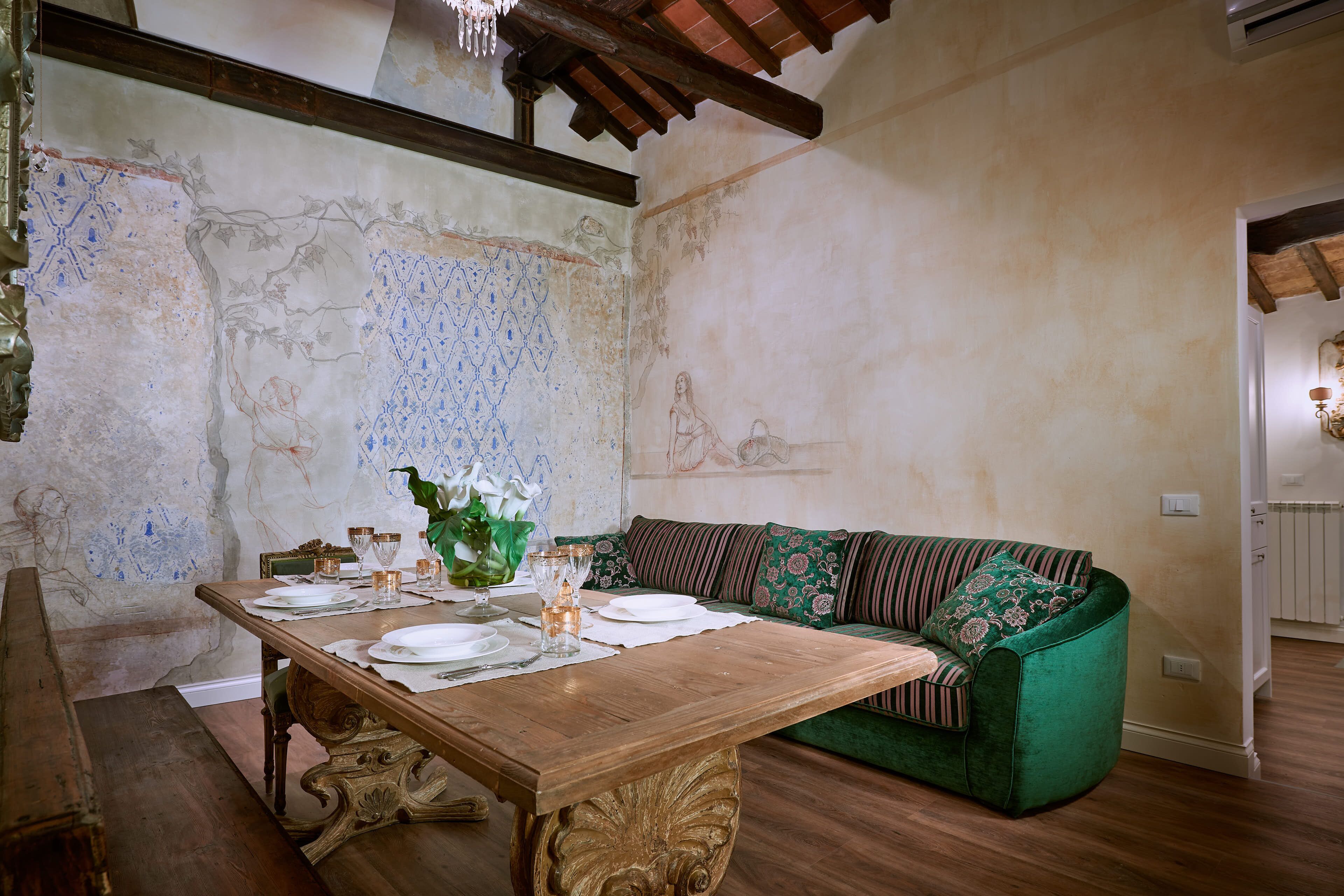 A dining area with a wooden table set for four, a green sofa, and a decorative vase.