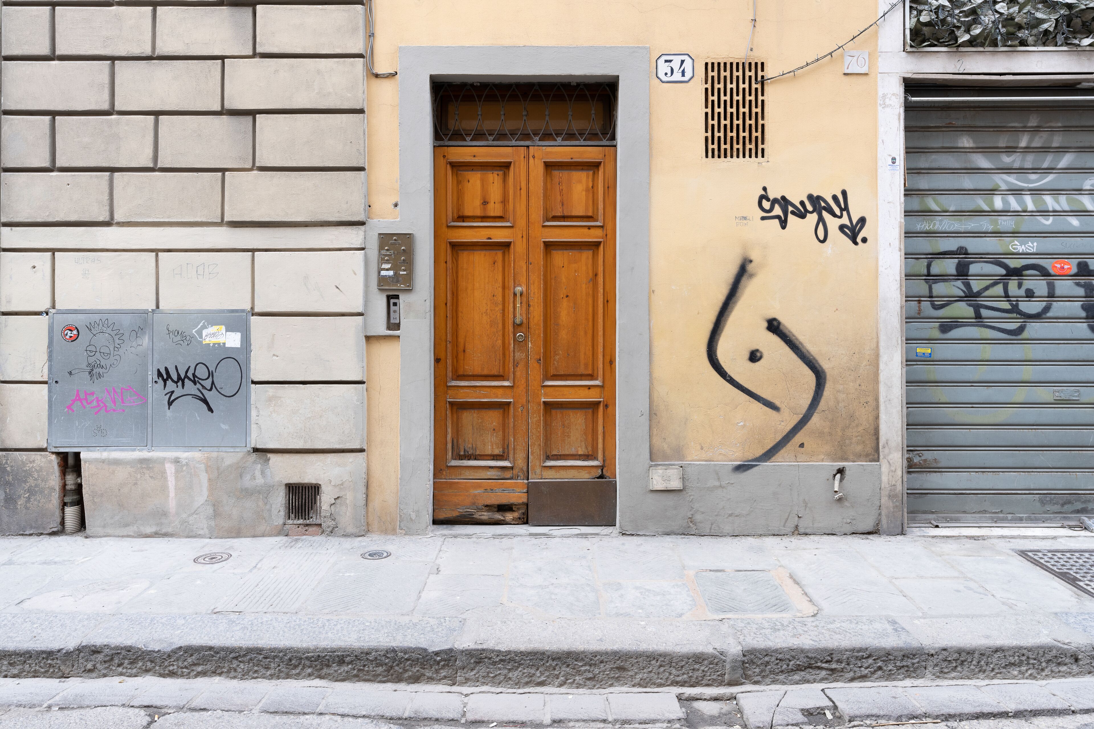 A building facade with a wooden double door, a metal shutter door, and a wall with graffiti.