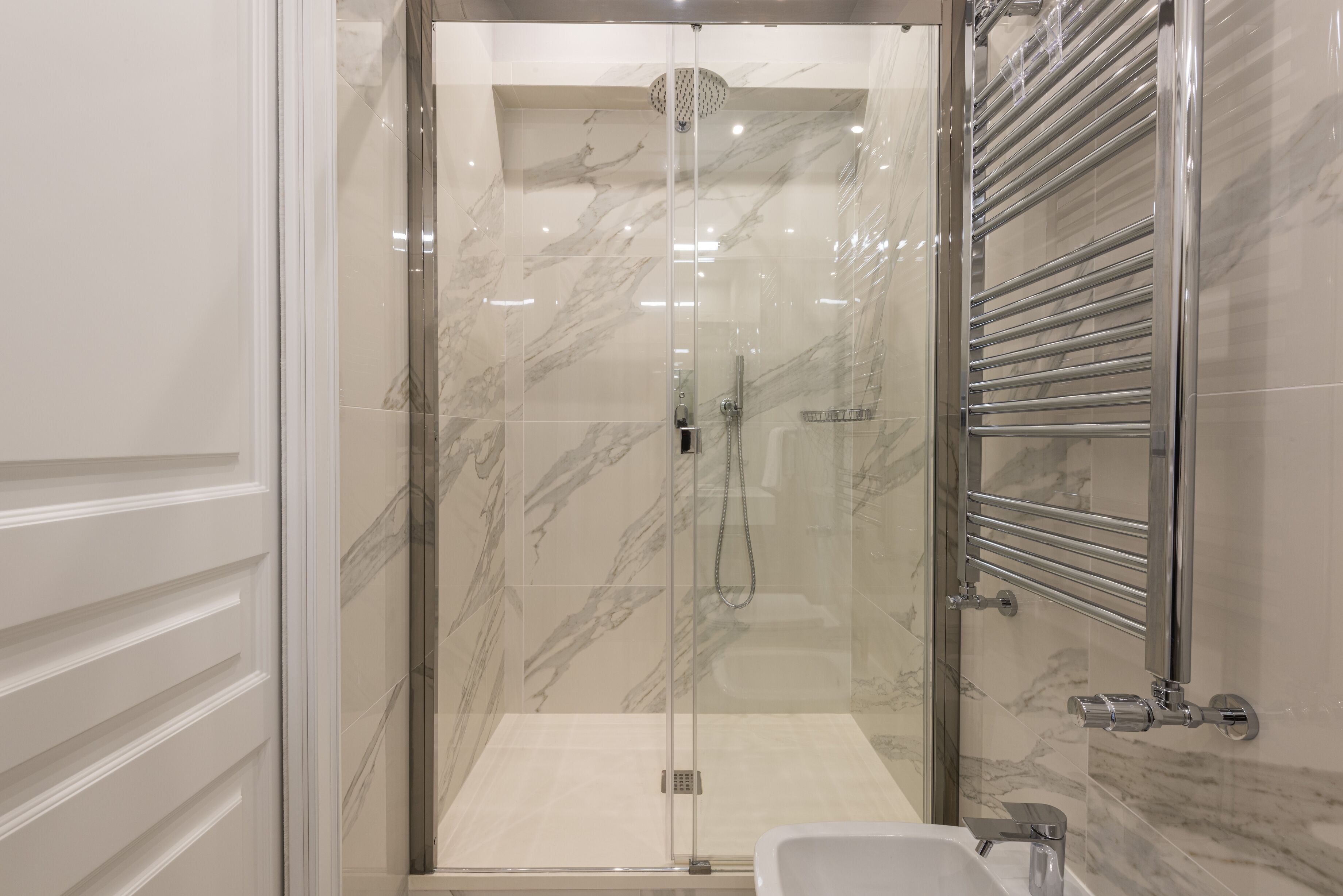 A modern bathroom with a glass-enclosed shower, a built-in sink, and a chrome towel rack.