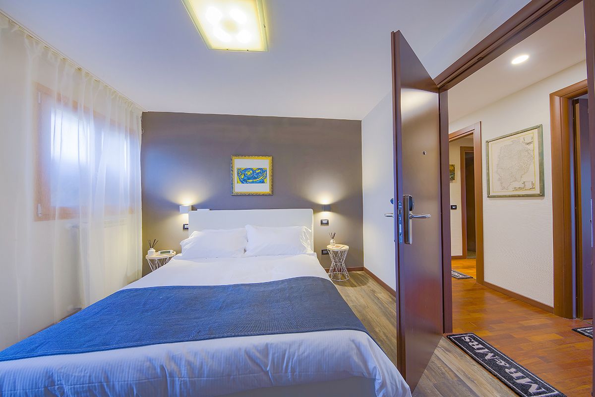 Una habitación de hotel con una cama grande, mesitas de noche, una obra de arte en la pared y una puerta que da a otra habitación.