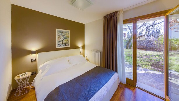 Une chambre avec un grand lit, une table de chevet, un tableau au mur et une vue sur l’extérieur grâce à une porte-fenêtre coulissante.