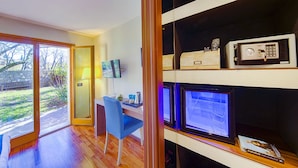 Une chambre moderne équipée d’un bureau, d’une chaise et d’un écran d’ordinateur. Un coffre-fort est fixé au mur, et une fenêtre offre une vue sur l’extérieur.