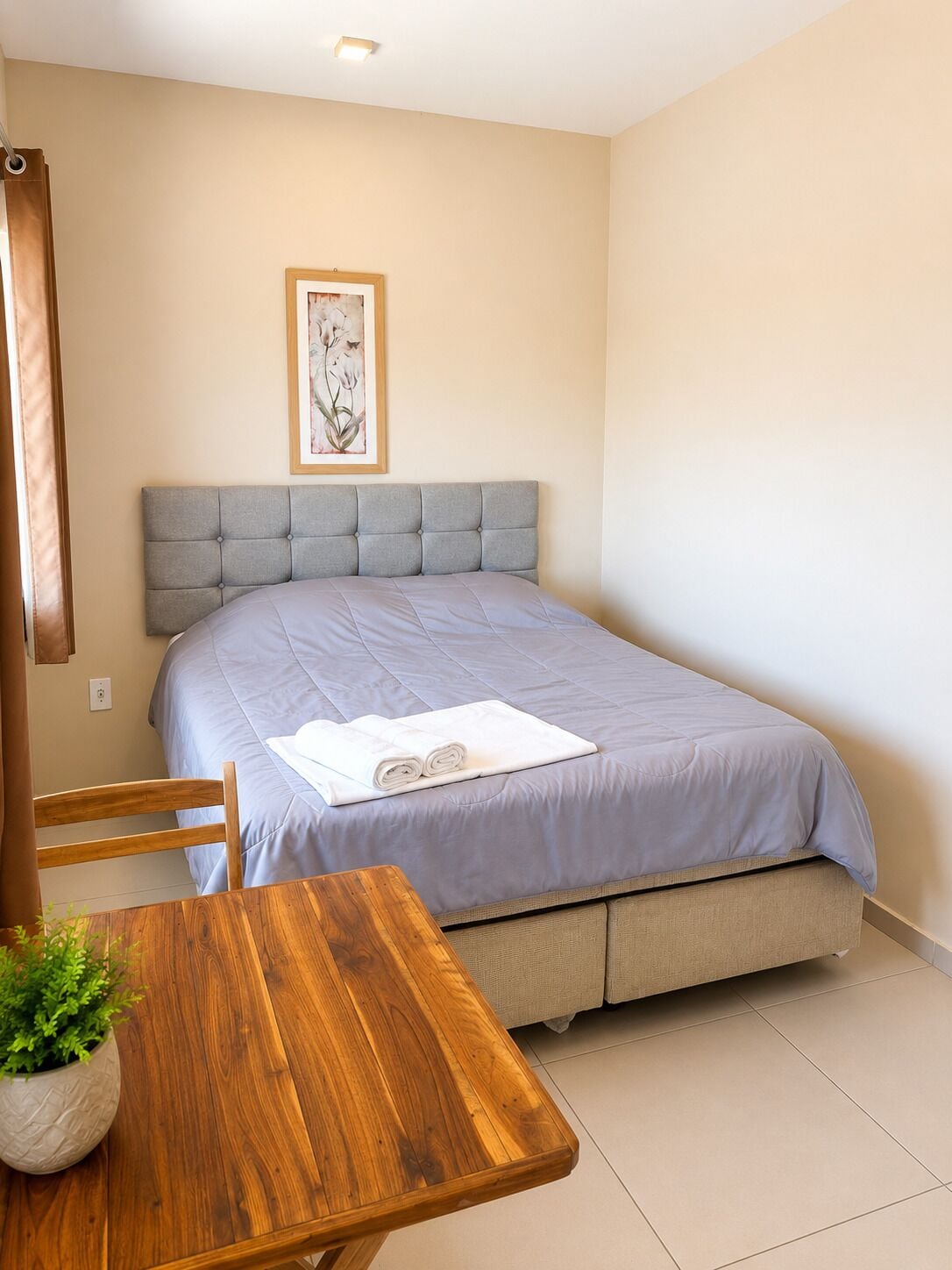 A bedroom with a bed, a wooden table with a plant, and a framed picture on the wall.