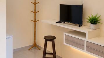 A modern room with a flat-screen TV on a white shelf, a wooden coat rack, a stool, and a potted plant.