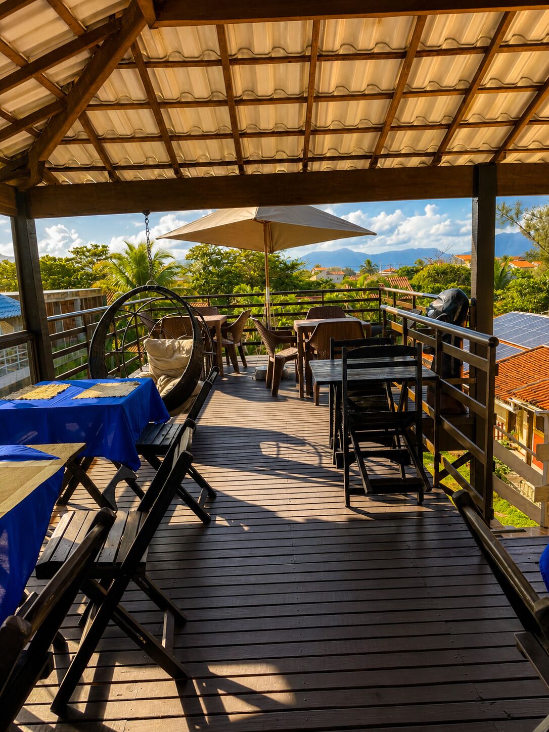 Terraza al aire libre con mesas y sillas, un sillón colgante y vistas del paisaje.