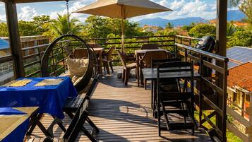 Terraza al aire libre con mesas y sillas, un sillón colgante y vistas del paisaje.