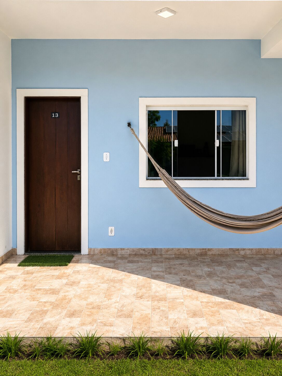 A modern building with a blue exterior, a wooden door marked with the number 13, a window with a white frame, and a hammock hanging over the entrance.