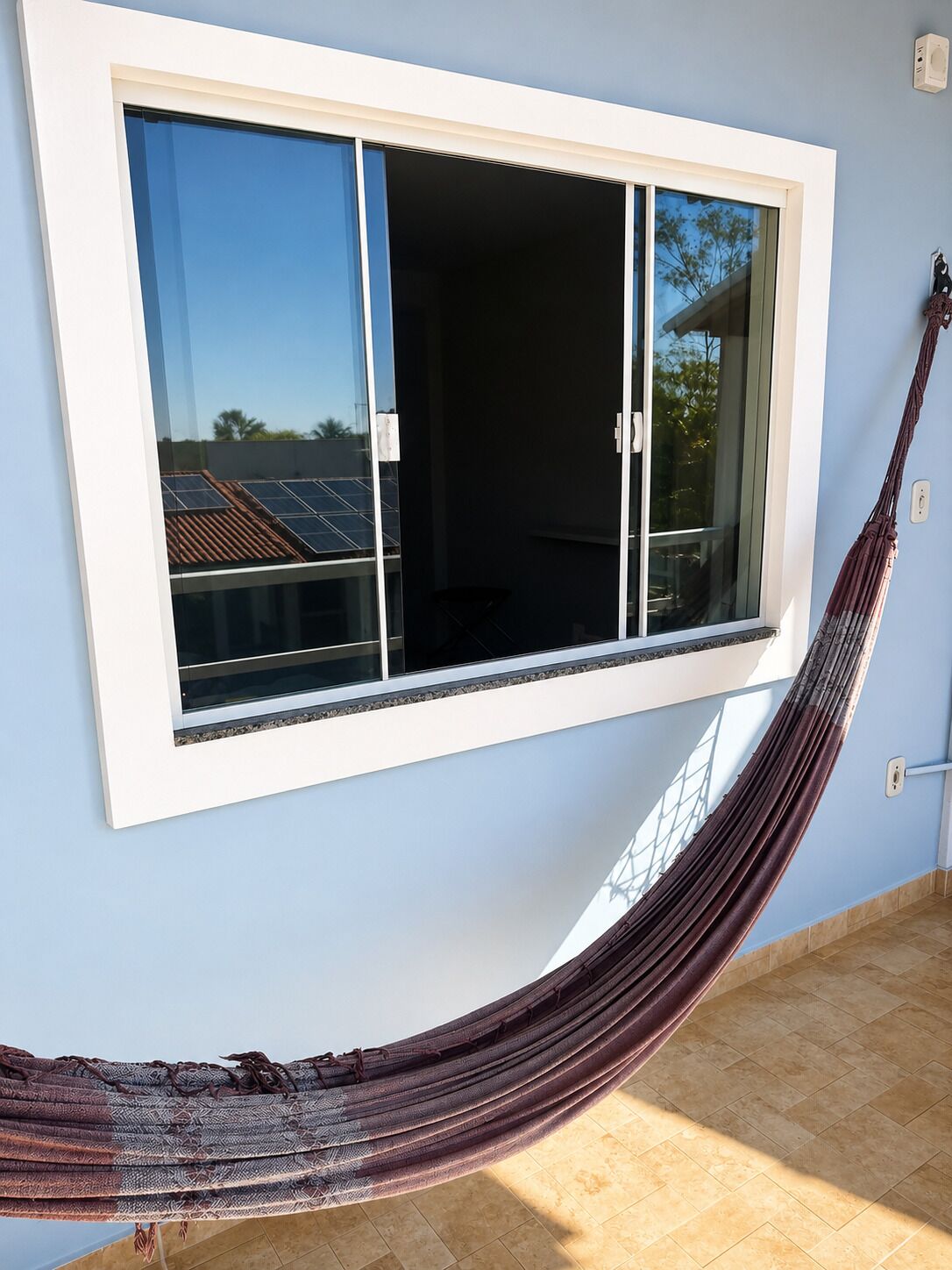 Ein Zimmer mit einem großen Fenster, einer Hängematte und Blick auf Solaranlagen.