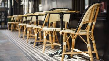 A row of wicker chairs and tables outside a building with a checkered floor pattern.