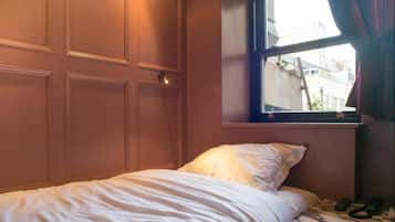 Een slaapkamer met een enkel bed, een raam met gordijnen en een deur.