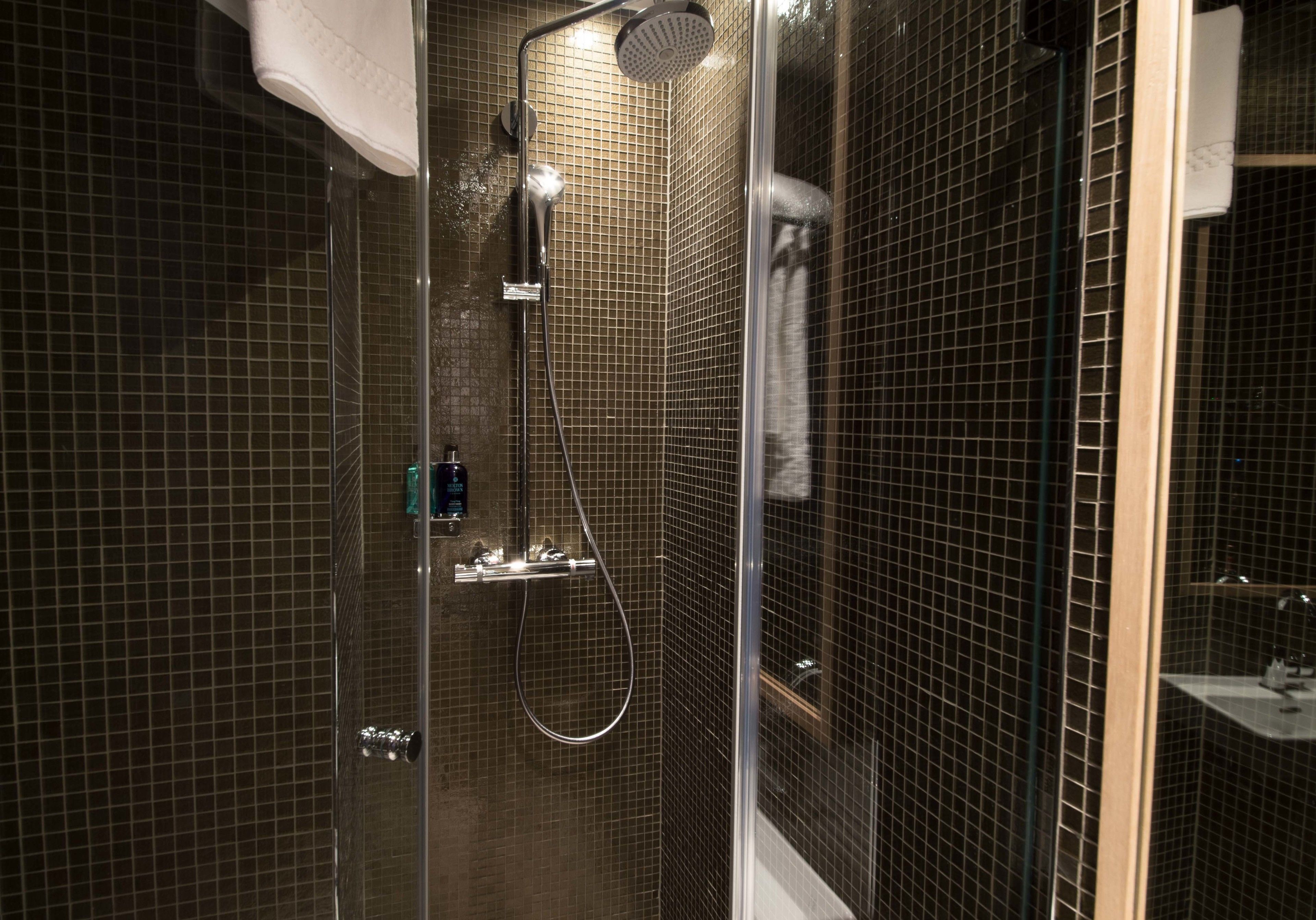 A modern shower with a glass door, a handheld showerhead, and a handheld showerhead.