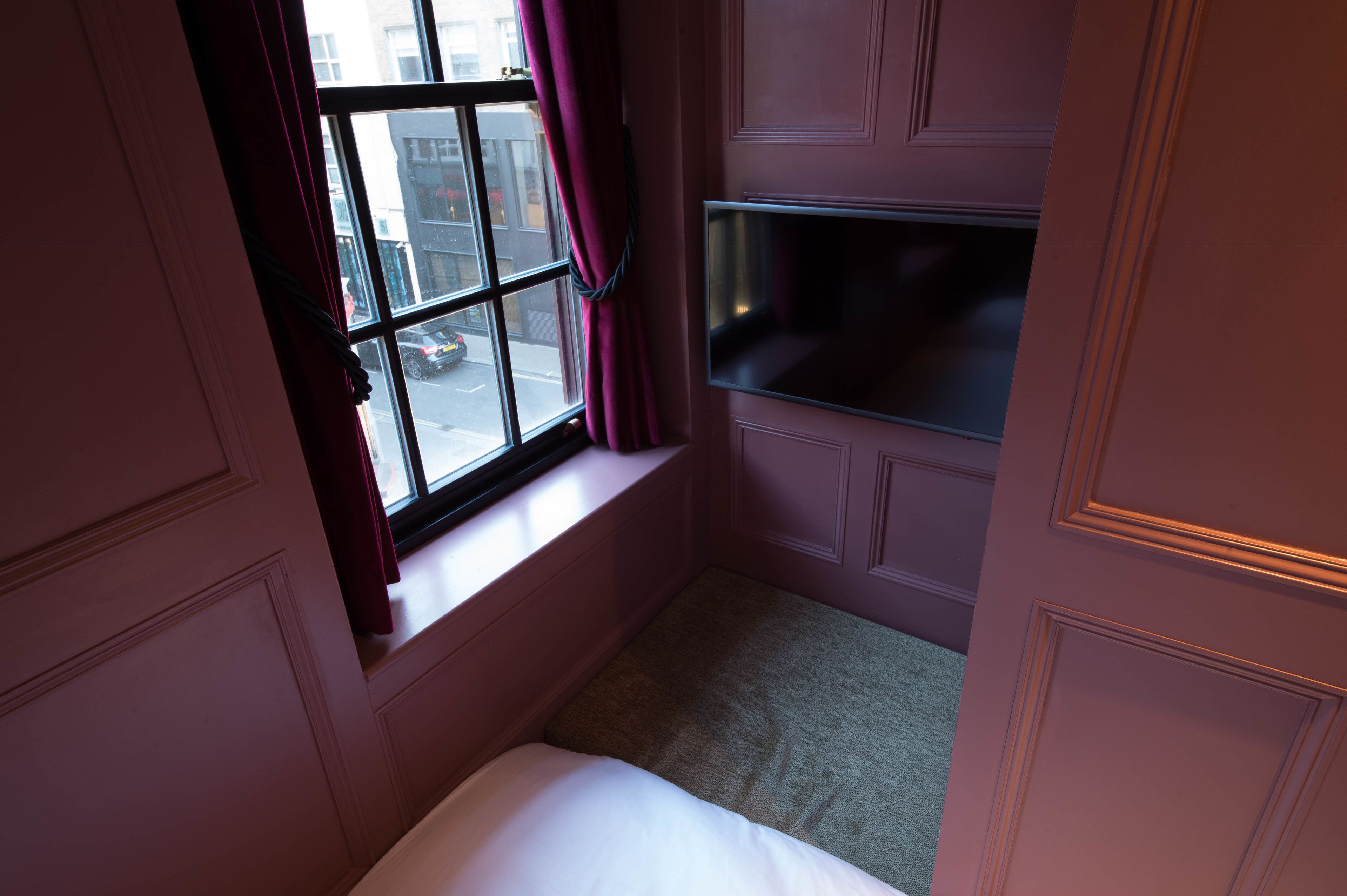 A bedroom with a window, a bed, and a TV mounted on the wall.