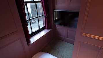 A bedroom with a window, a bed, and a TV mounted on the wall.