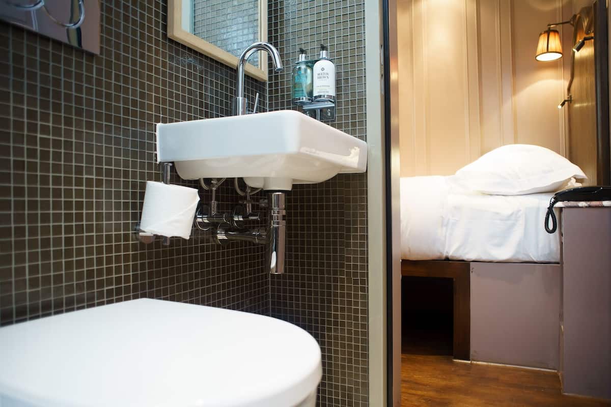 Un baño con un lavamanos blanco, un inodoro y una cama con ropa de cama blanca.