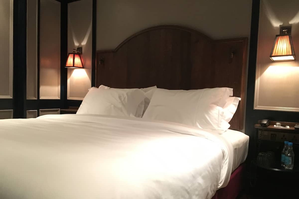 Una cama bien hecha con sábanas blancas, cabecero de madera y dos lámparas de pared a cada lado.