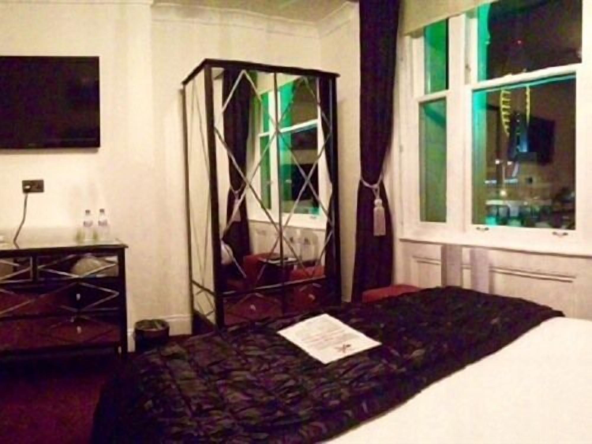 Een hotelkamer met een bed, een bureau, een stoel, een raam met gordijnen en een aan de muur bevestigde televisie.