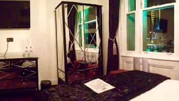 Een hotelkamer met een bed, een bureau, een stoel, een raam met gordijnen en een aan de muur bevestigde televisie.