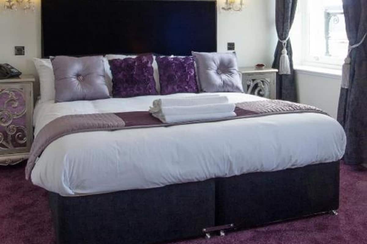 Une chambre avec un grand lit, un lustre et des motifs floraux violets décorant les murs.