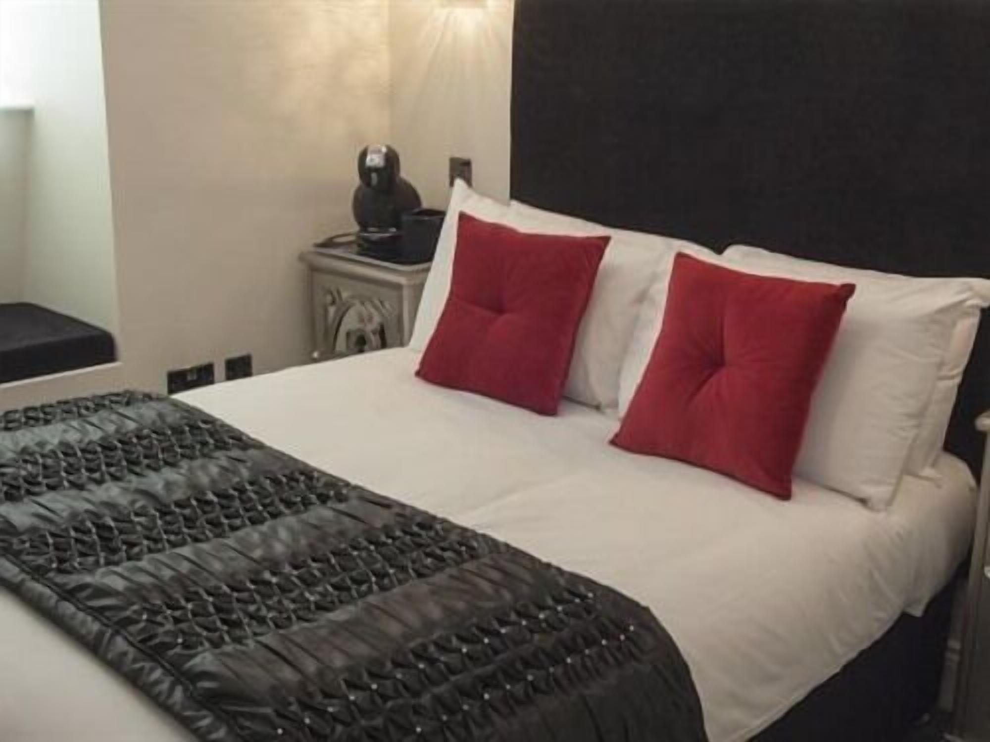 A neatly made bed with a black quilt and two red pillows, a white headboard, and a small bedside table with a lamp.