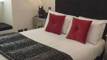 A neatly made bed with a black quilt and two red pillows, a white headboard, and a small bedside table with a lamp.