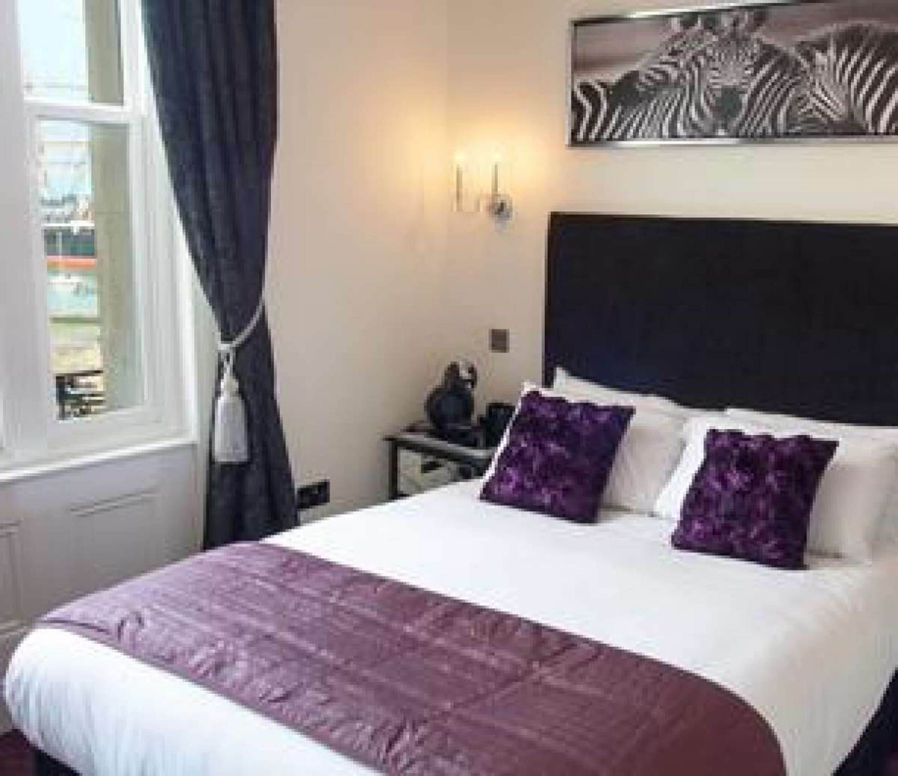 Un dormitorio con cama, mesita de noche, lámpara y ventana con cortinas.