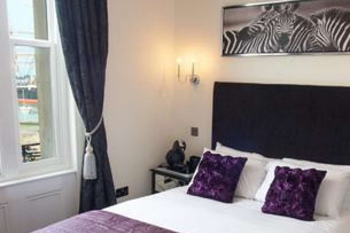 Une chambre à coucher avec un lit, une table de chevet, une lampe et une fenêtre avec des rideaux.